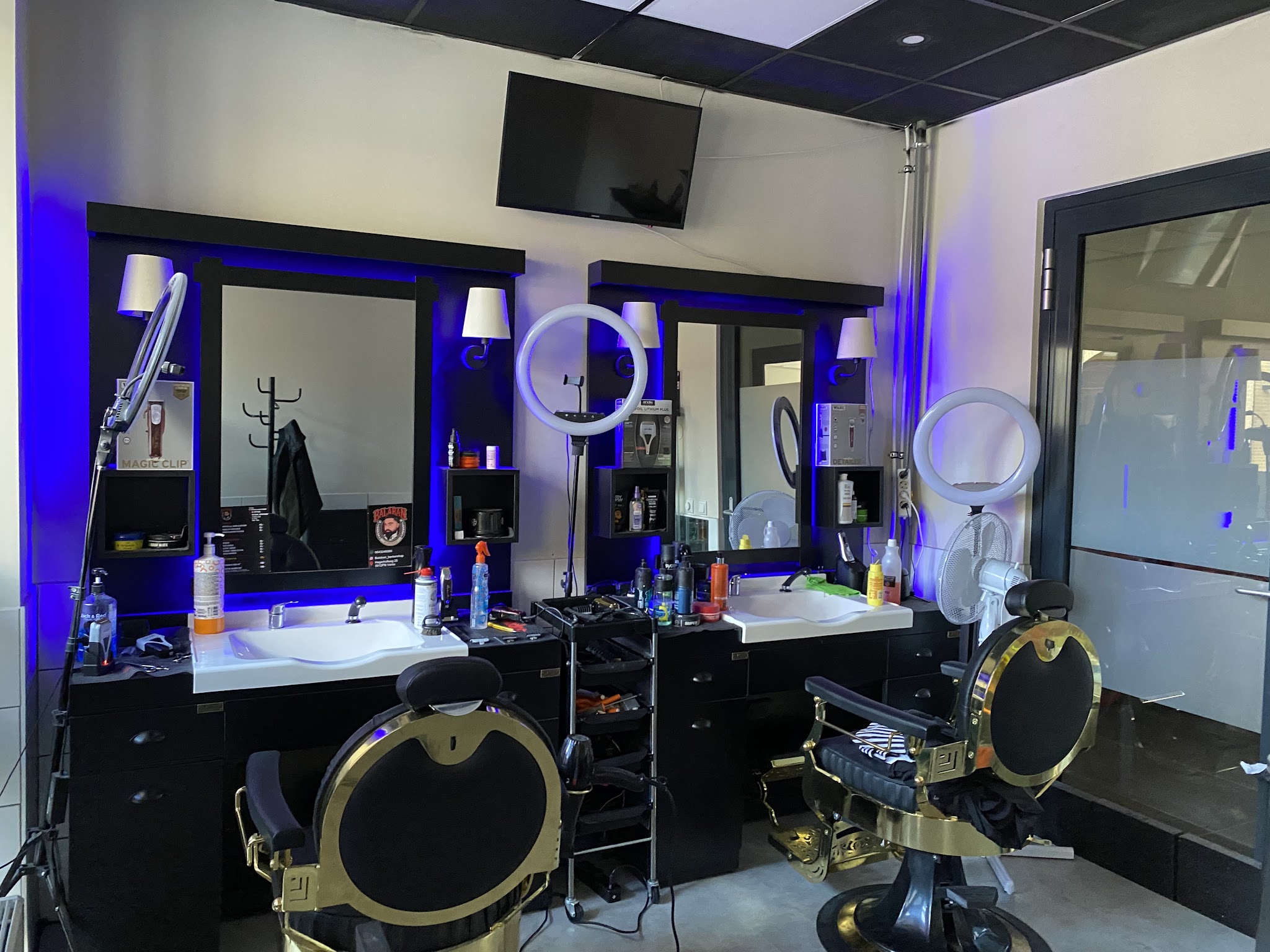 Het interieur van Balaban barber: kappersstoelen in zwart en goud voor spiegels met blauw licht